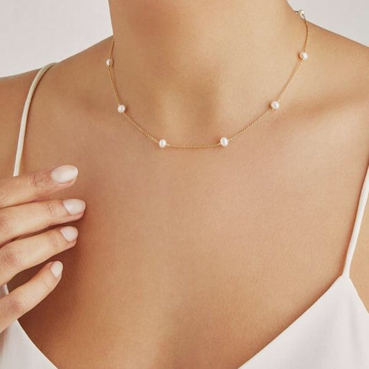 Gold necklace with pearls on a person wearing a white top against a light background