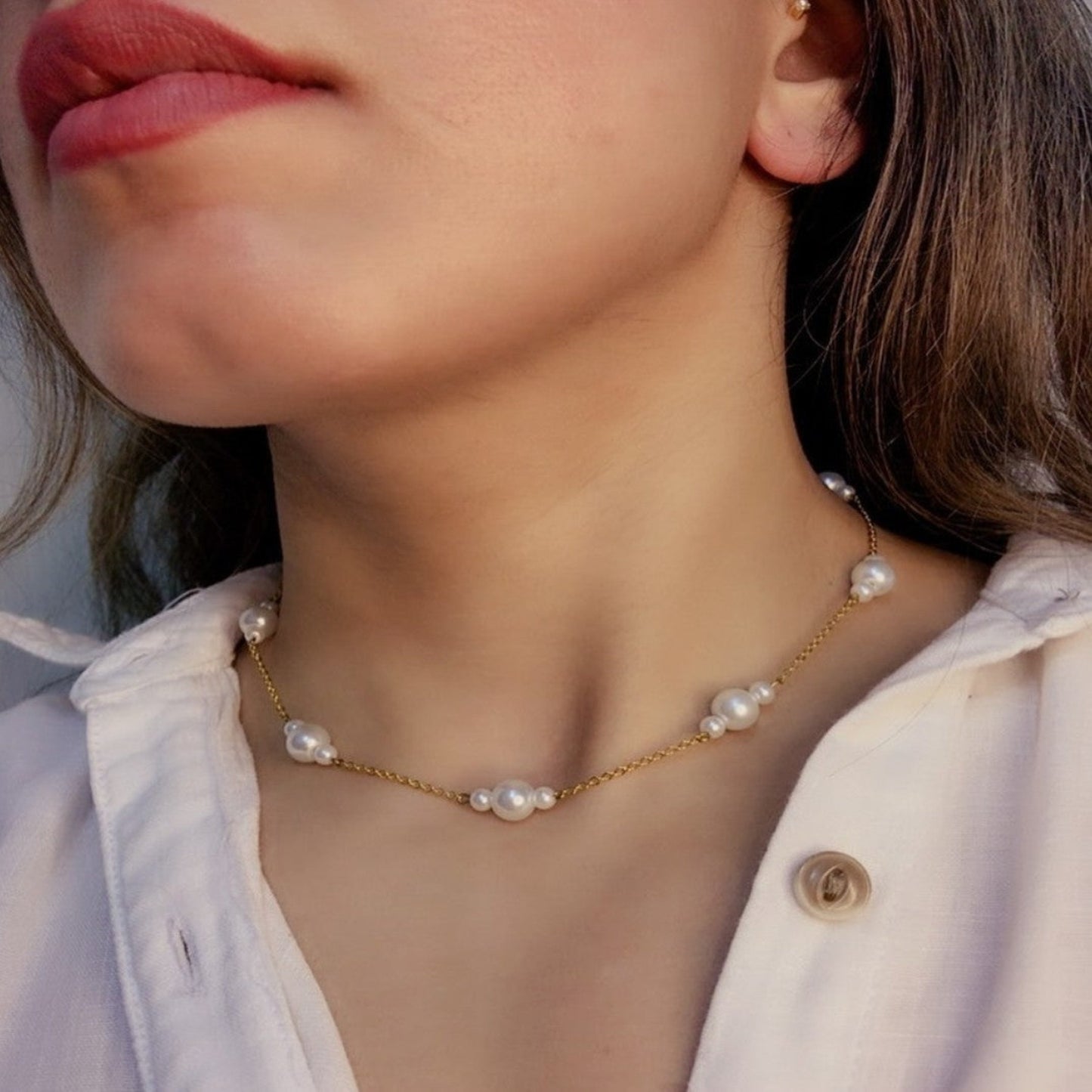 Close-up of a person wearing a pearl necklace with a neutral background