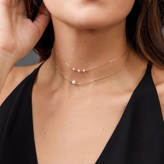 Close-up of a woman wearing a delicate gold necklace with a black top.