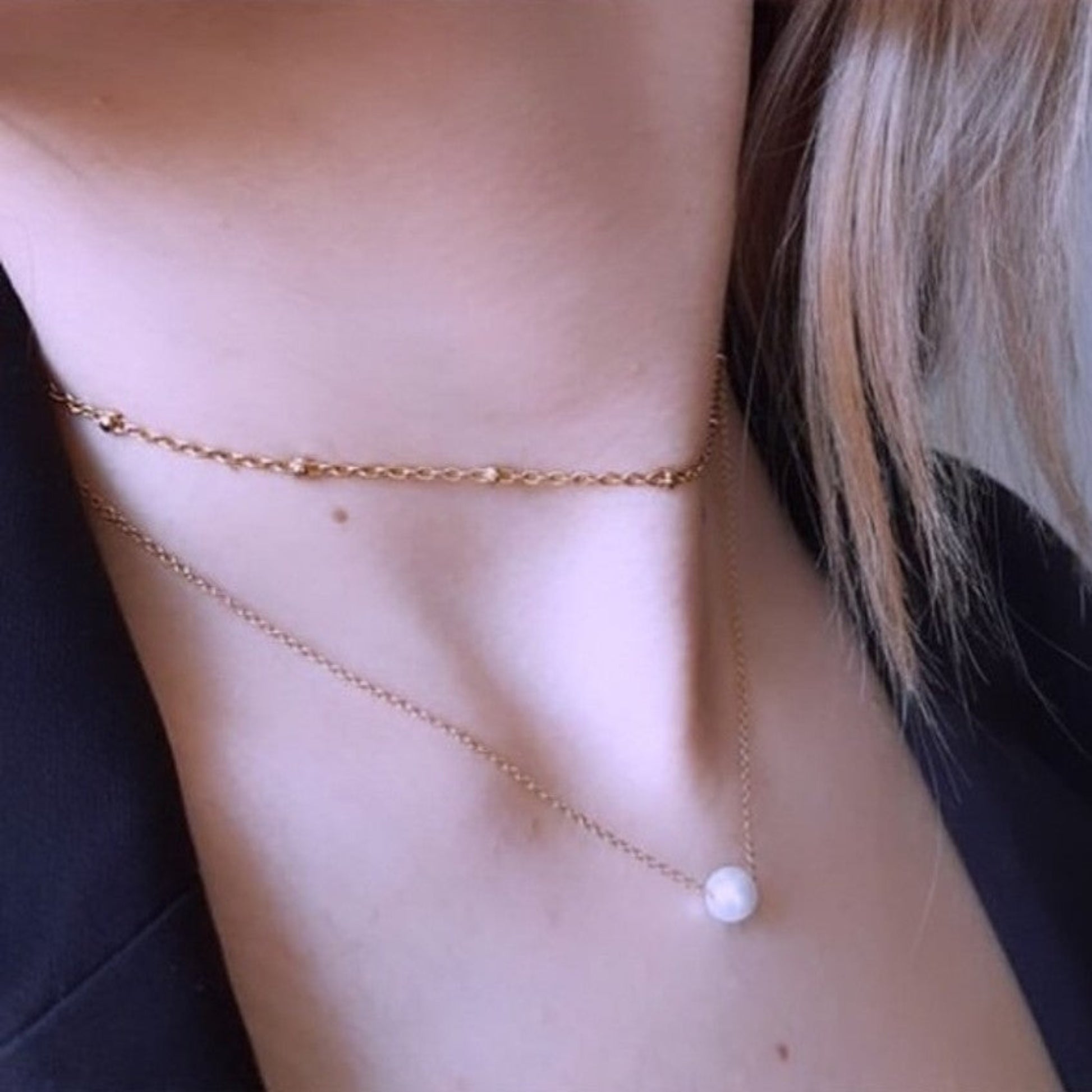 Gold necklace with a pearl pendant on a person wearing a black top.