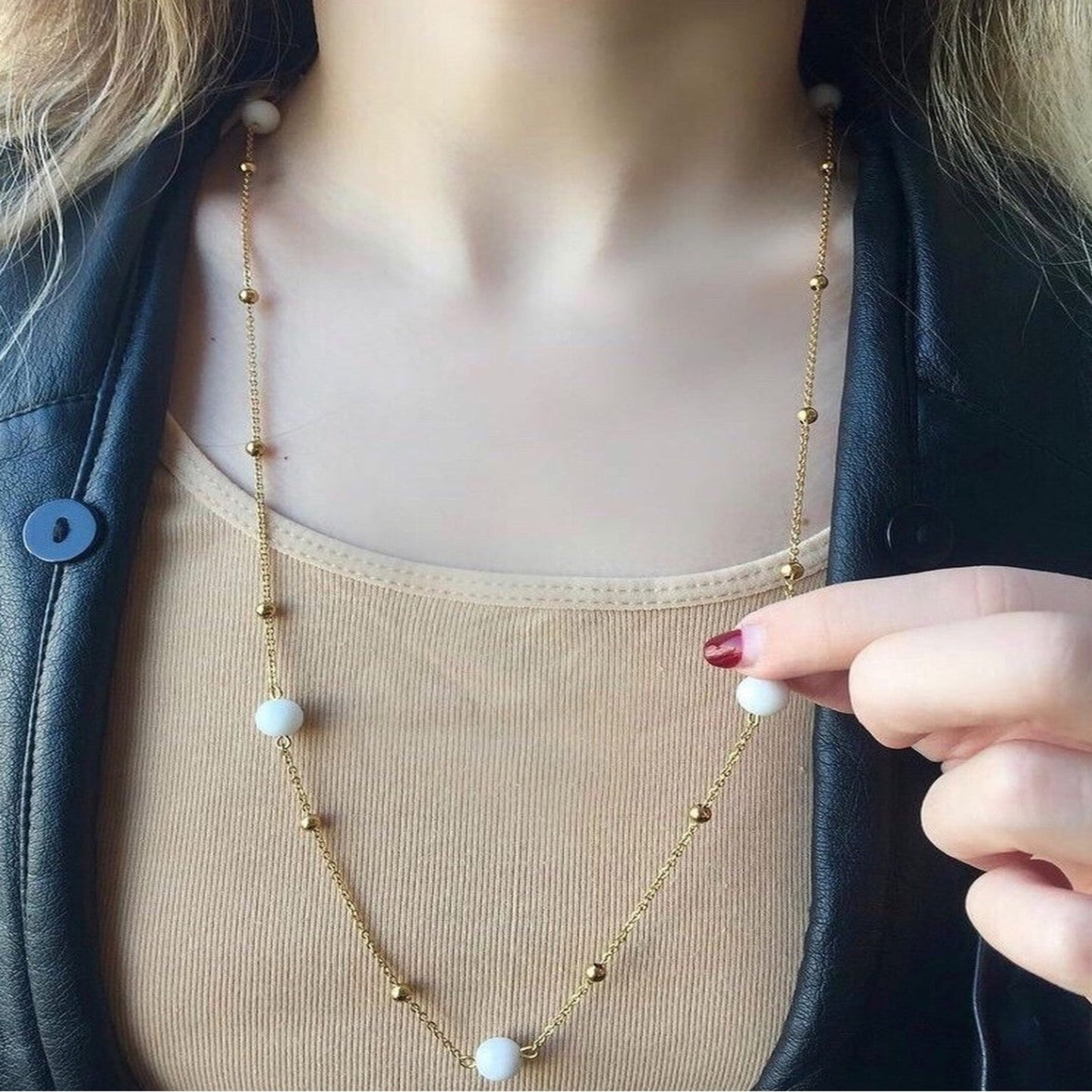 Person wearing a long necklace with white beads and gold chain, held by a hand.