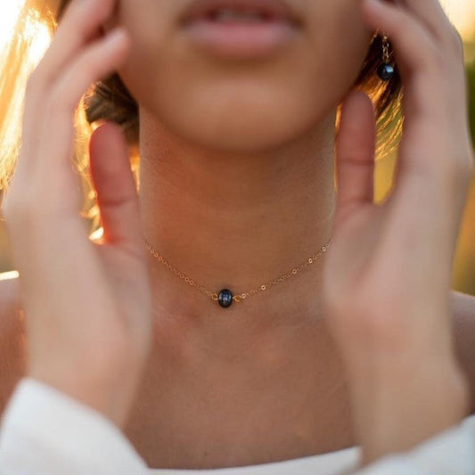 Person wearing a delicate necklace with a small black bead, hands adjusting it.