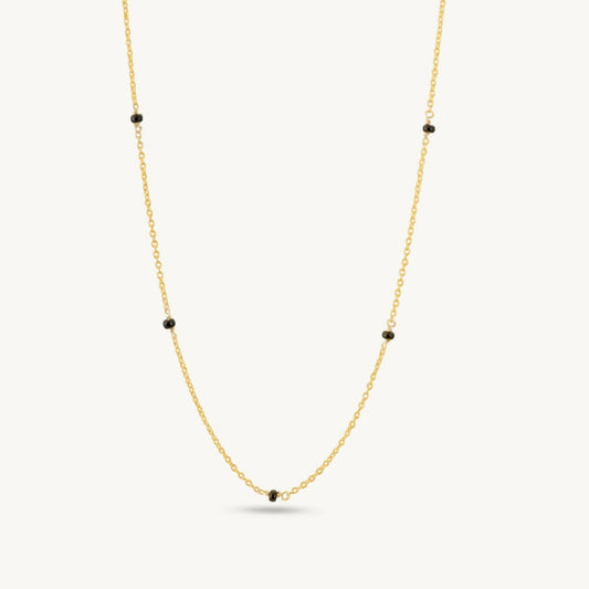 Gold necklace with black beads on a white background