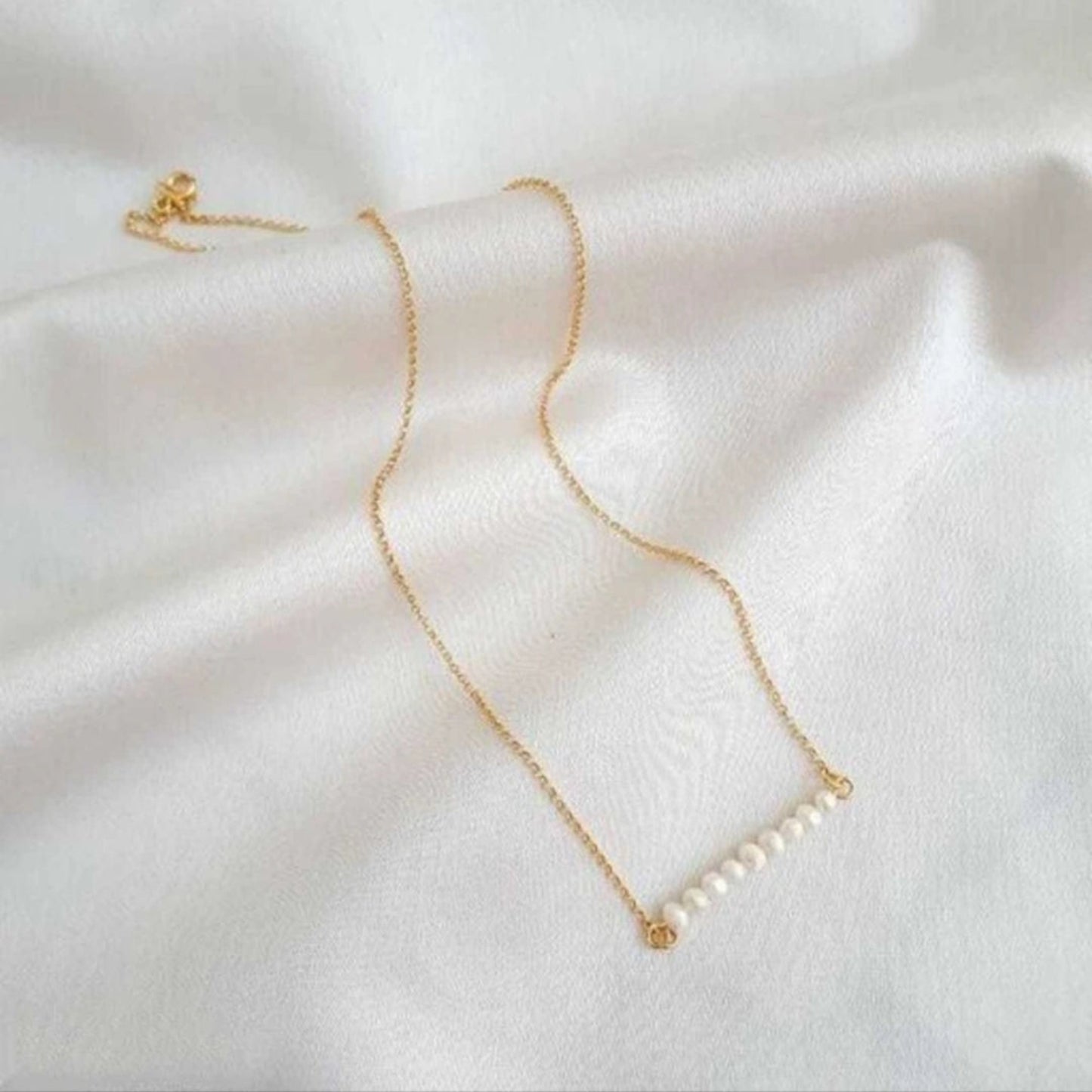 Gold necklace with pearls on a white fabric background