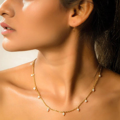 Close-up of a woman wearing a gold necklace with small pearls.
