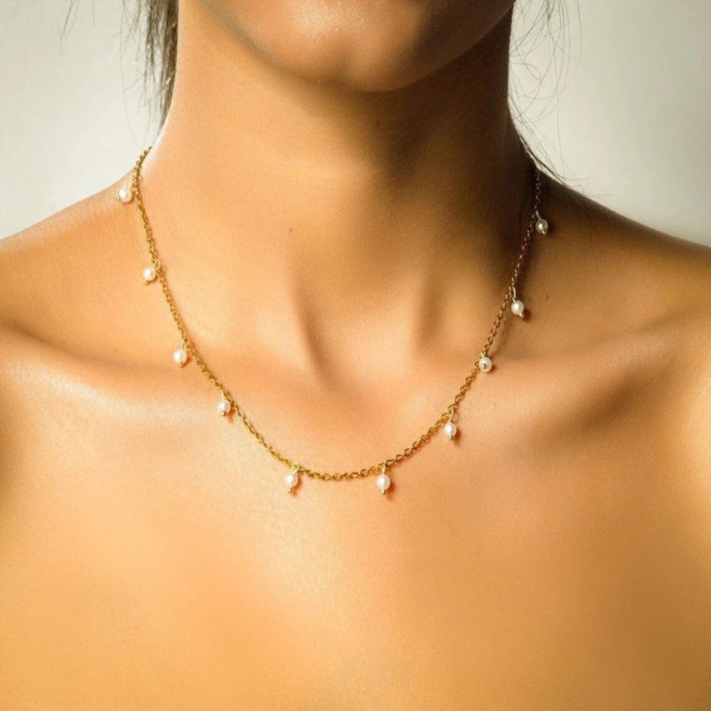 Close-up of a gold necklace with pearl-like beads on a person's neck.