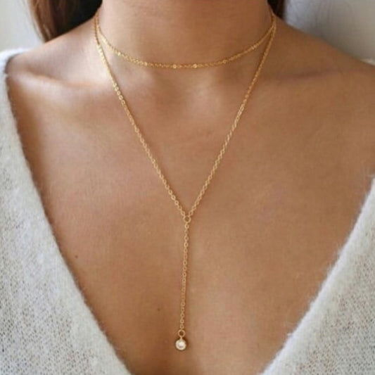 Gold necklace with a pendant on a person wearing a white top.