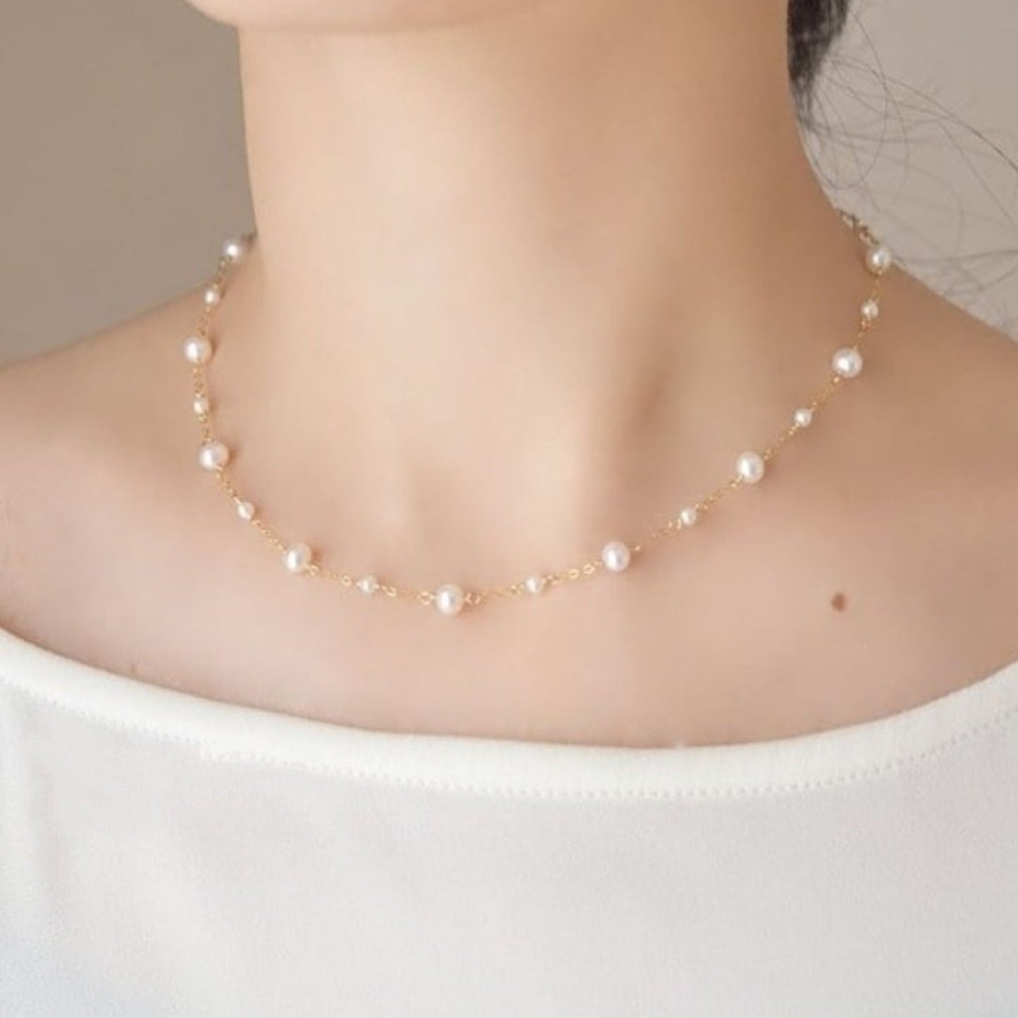 Pearl necklace worn by a person on a plain background