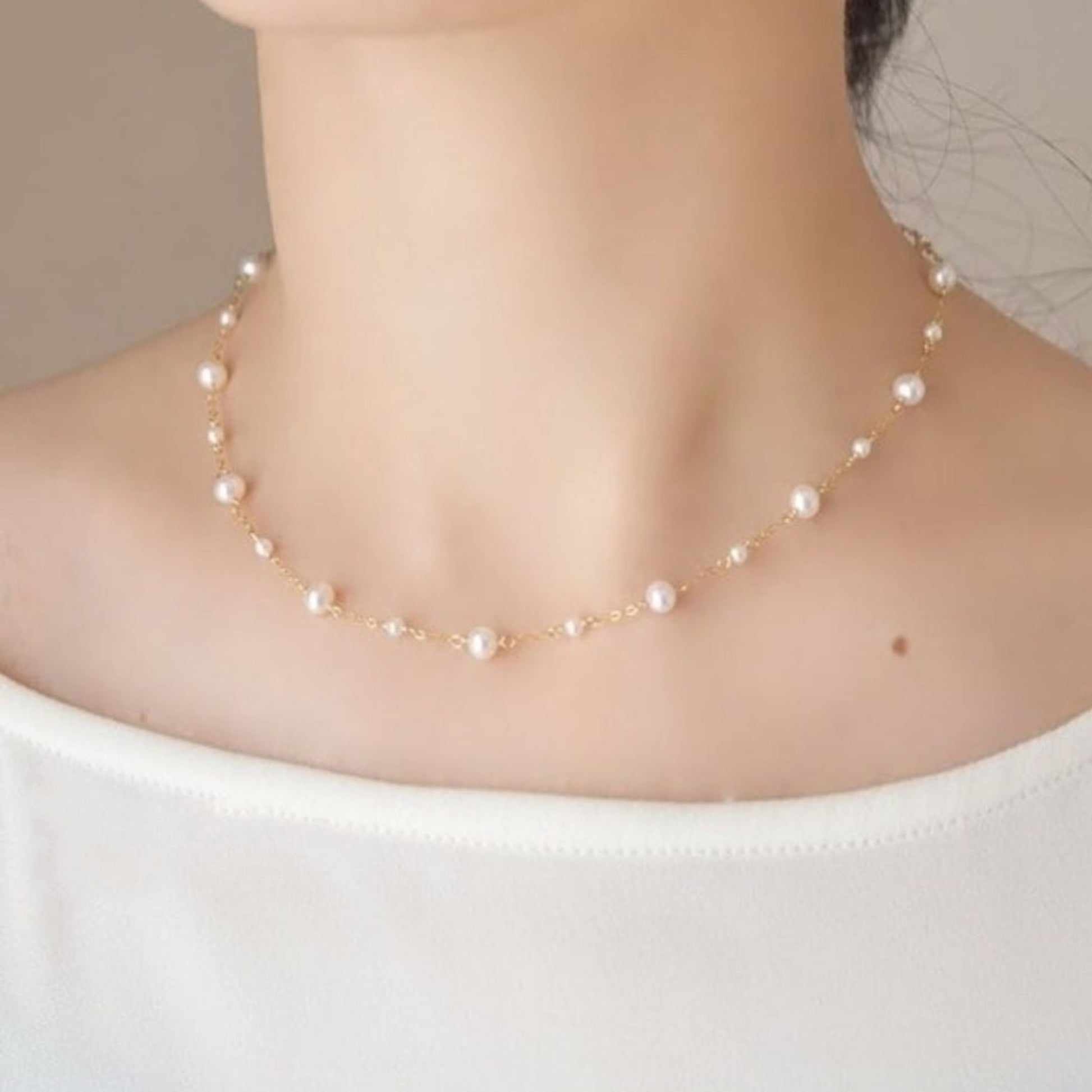 Pearl necklace worn by a person on a plain background