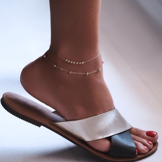 Silver sandal worn on a foot with a plain background
