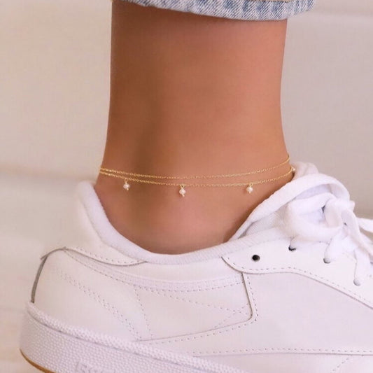 Gold anklets on a person's ankle with a white sneaker