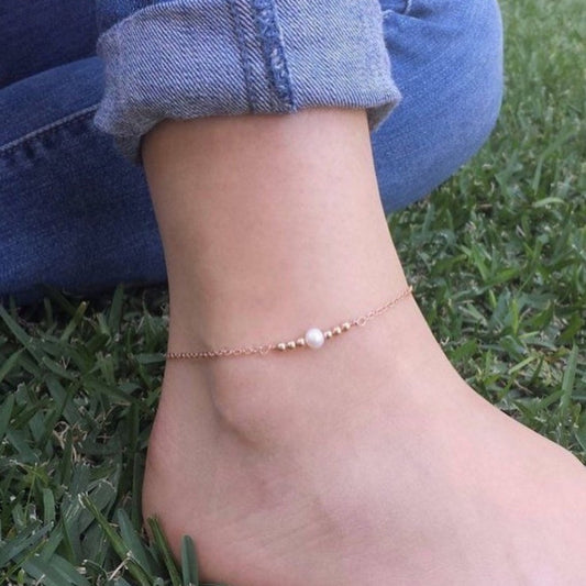 Ankle bracelet with a pearl on a person's ankle against a grass background