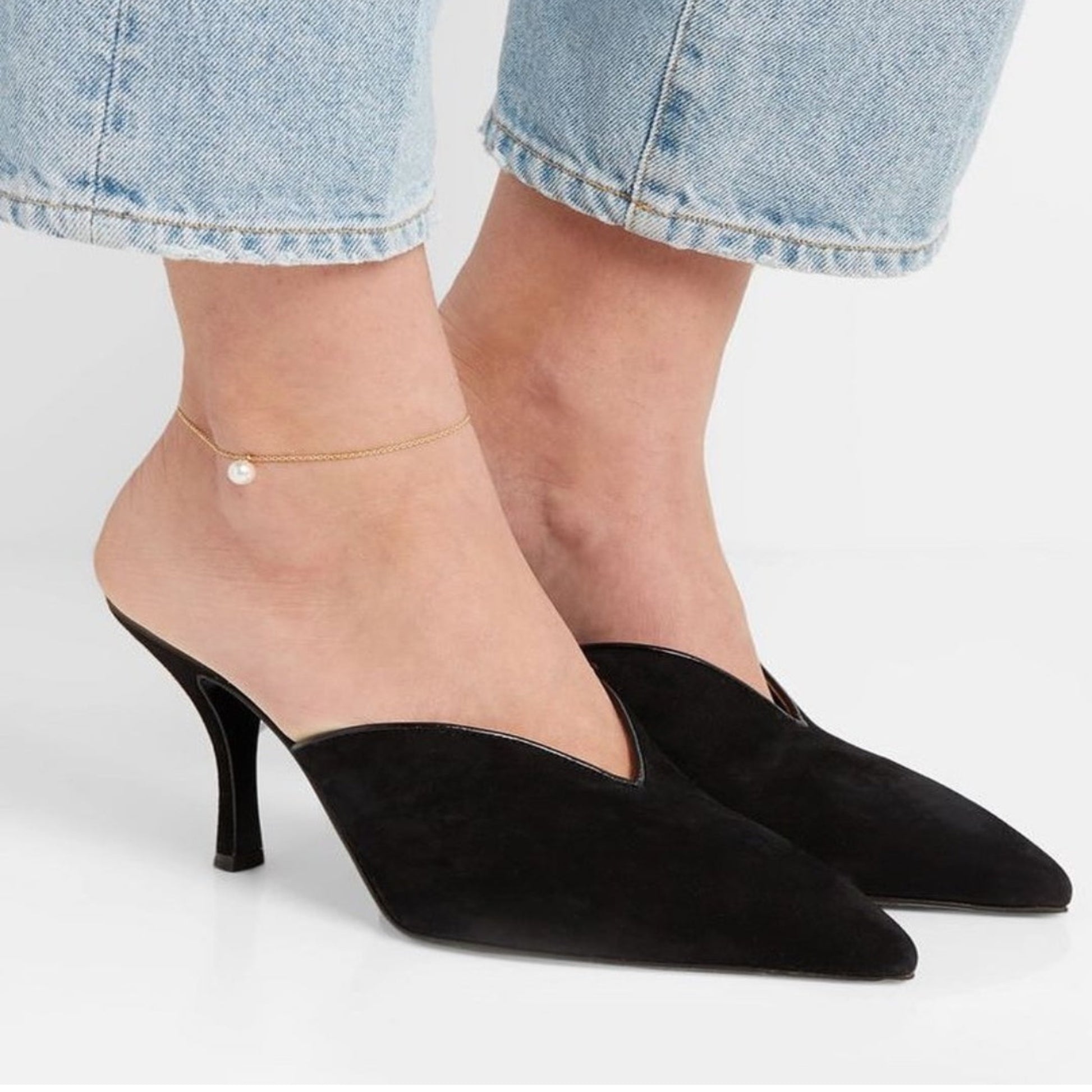 Black high-heeled shoes worn with light blue jeans on a neutral background