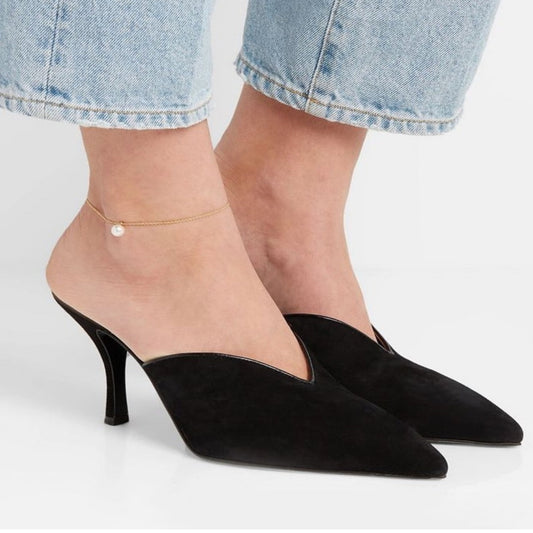 Black high-heeled shoes worn with light blue jeans on a neutral background