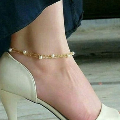 Gold anklet with pearls on a foot wearing a high-heeled shoe.