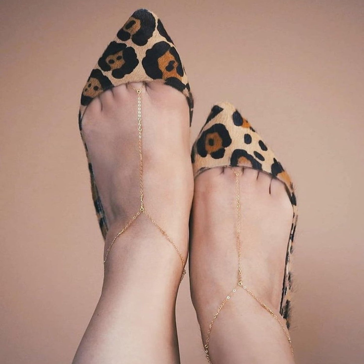 Leopard print shoes with sheer tights and a gold anklet on a beige background