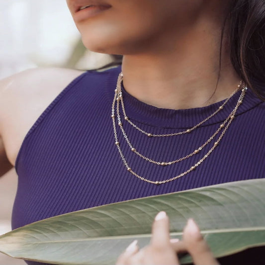 Person wearing a gold necklace with a purple top, holding a large green leaf.