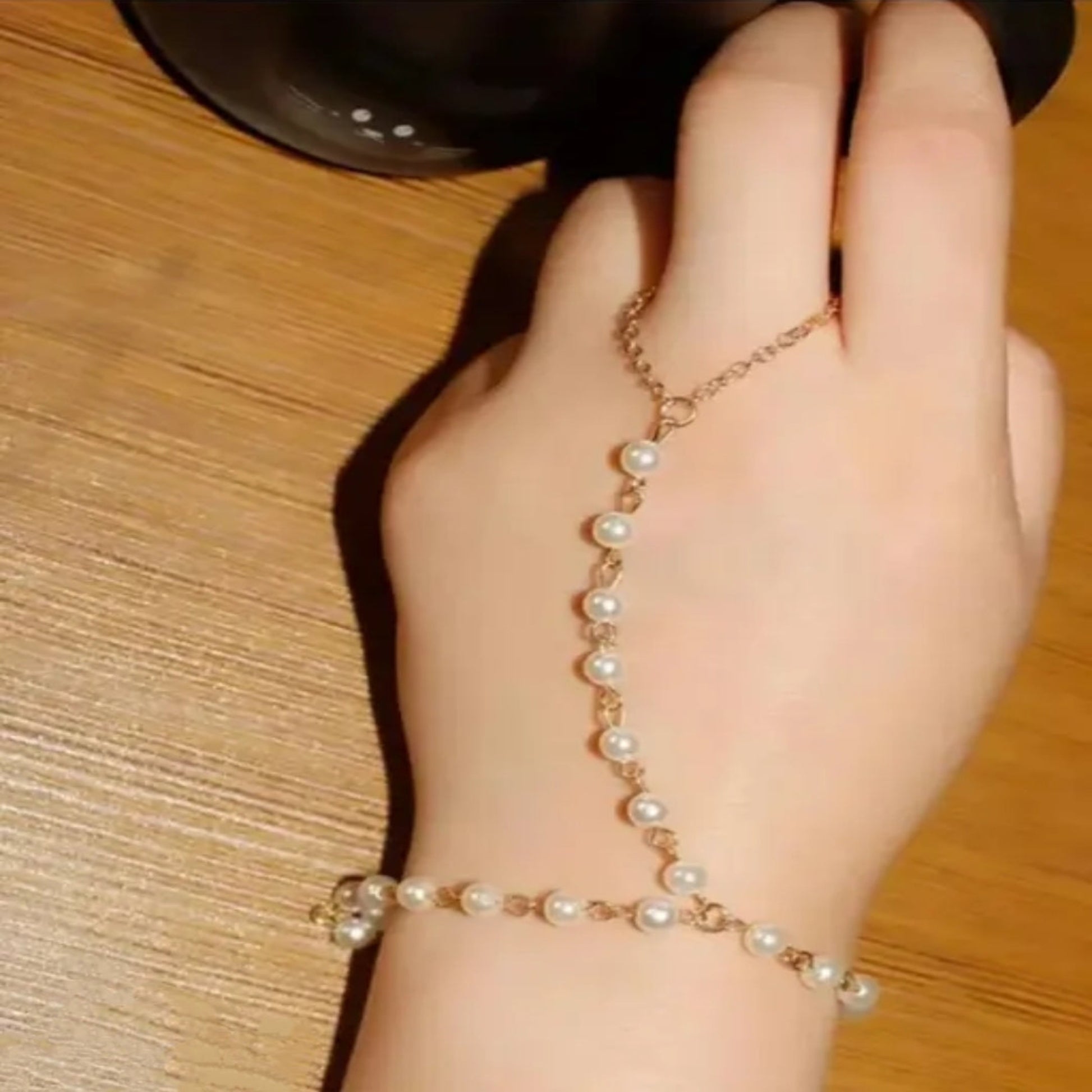 Hand wearing a pearl bracelet on a wooden surface
