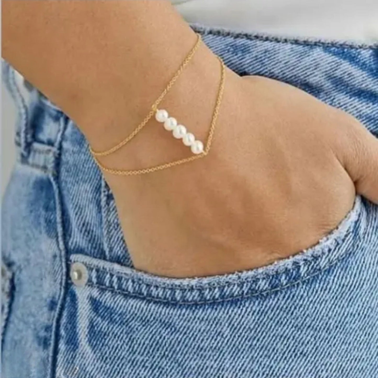 Gold anklet with pearls on a person's ankle against a denim background
