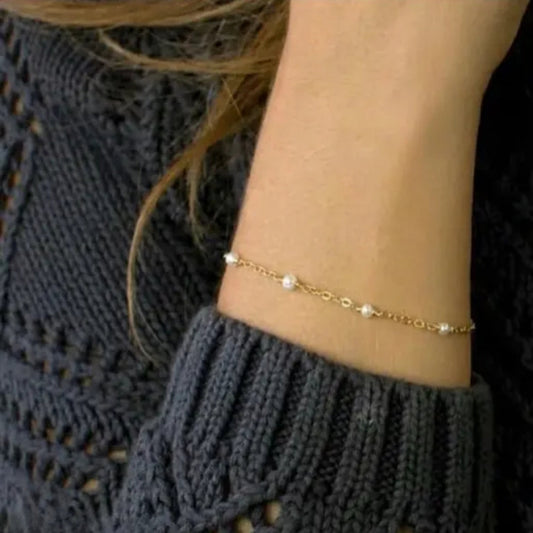 Gold anklet with pearls on a person wearing a dark gray knit sweater.