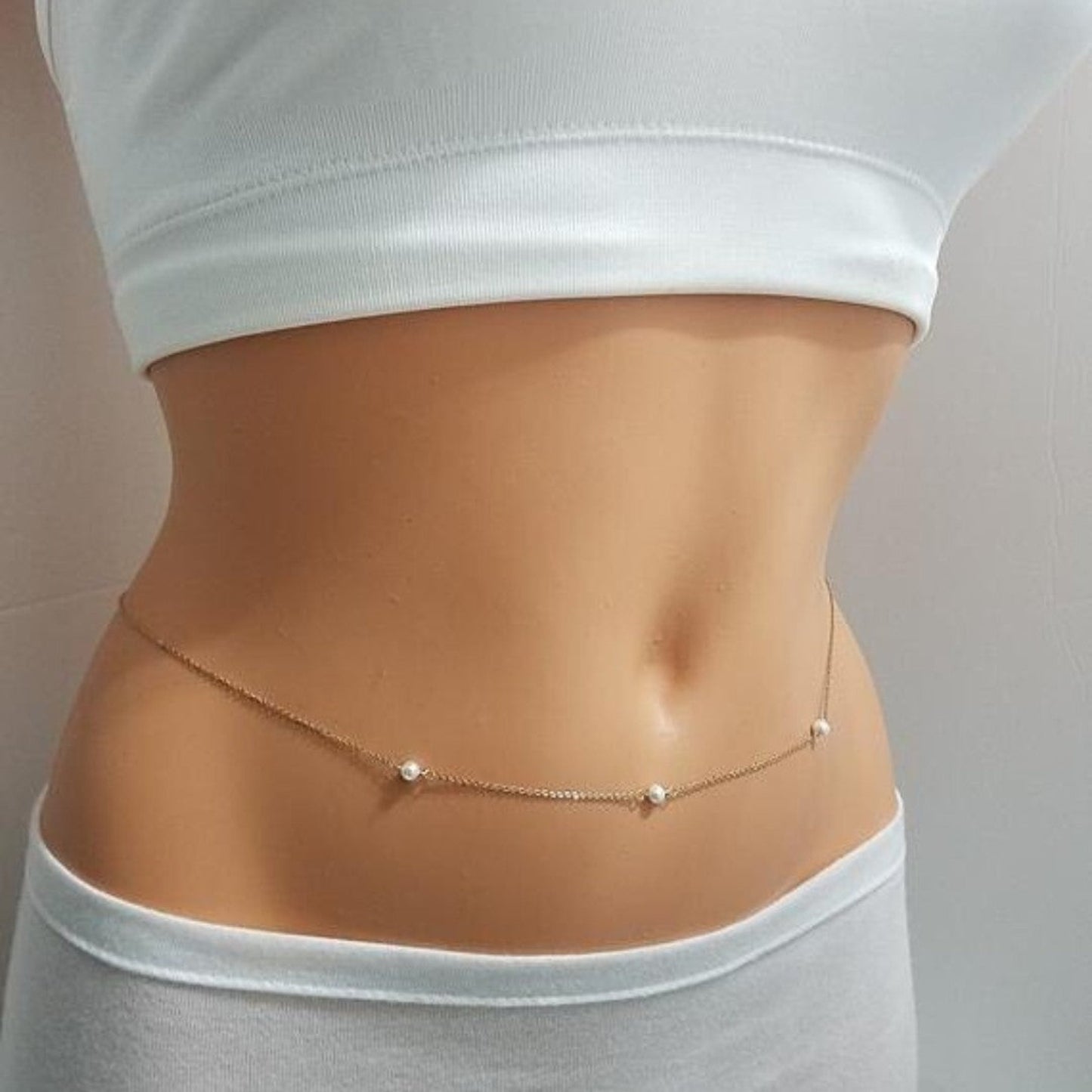 Person wearing a thin gold chain with small pearls around the waist on a plain background