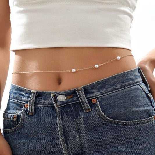 Person wearing a pearl belt around their waist with a white top and blue jeans.
