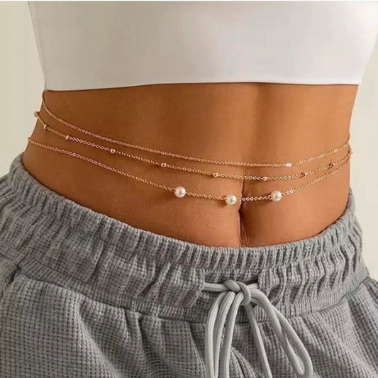 Person wearing a gold chain belt with pearls on a plain background