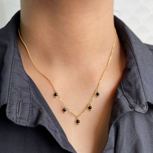 Gold necklace with black beads worn by a person against a neutral background
