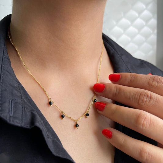 Gold necklace with black beads worn by a person with red nail polish.