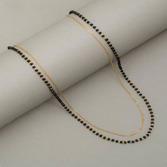 Necklace with black beads and gold chain on a light gray background