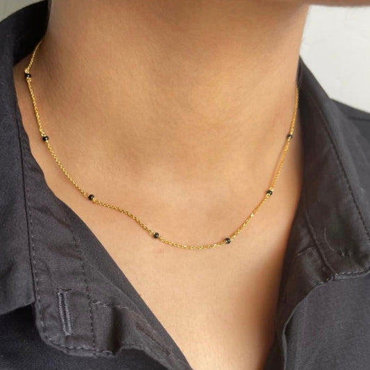 Gold necklace with small black beads worn by a person against a neutral background