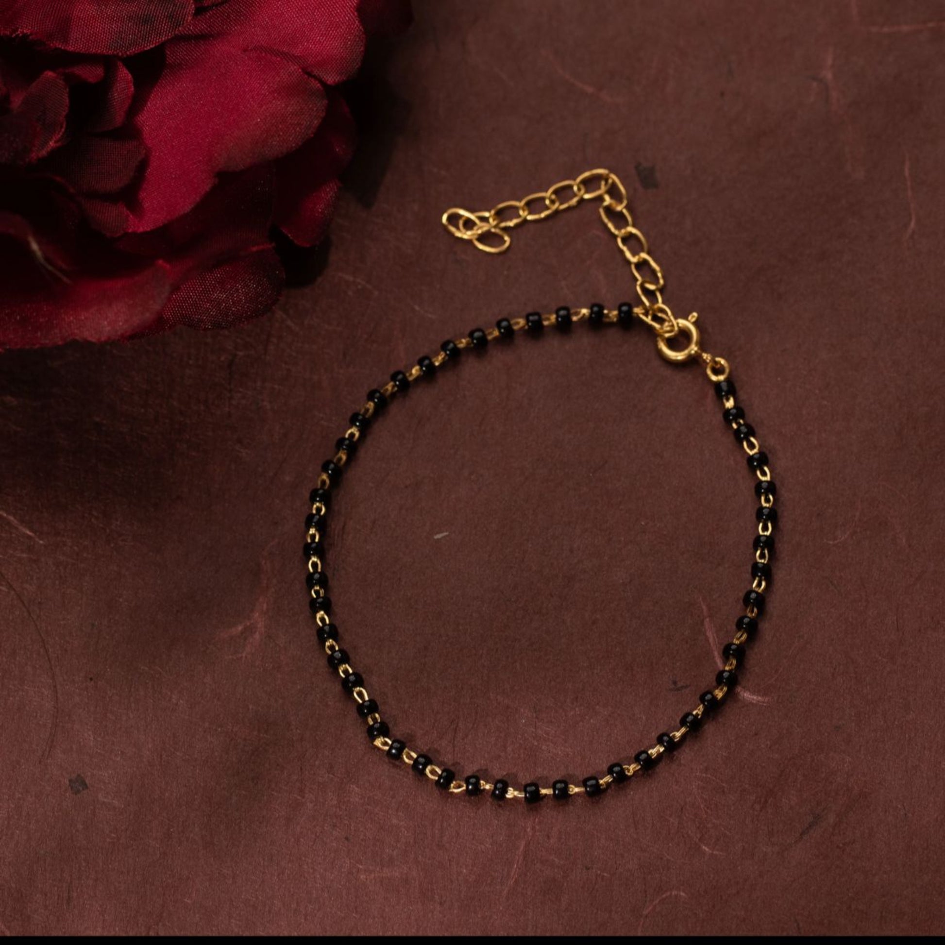 Gold and black beaded necklace on a brown surface with a red flower.
