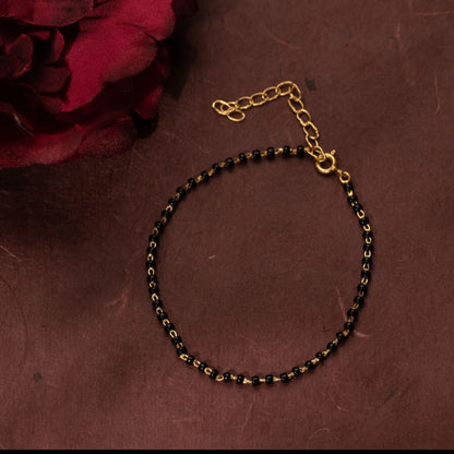 Gold and black beaded necklace on a brown surface with a red flower.