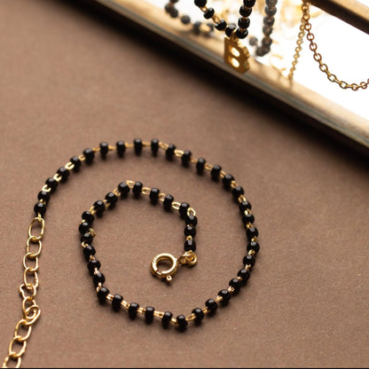 Black beaded necklace with gold chain on a brown surface