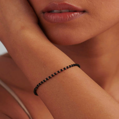 Close-up of a person's arm wearing a black beaded bracelet with a neutral background