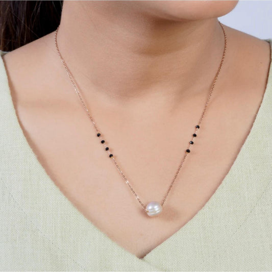 Necklace with a pearl pendant worn by a person in a light green top.