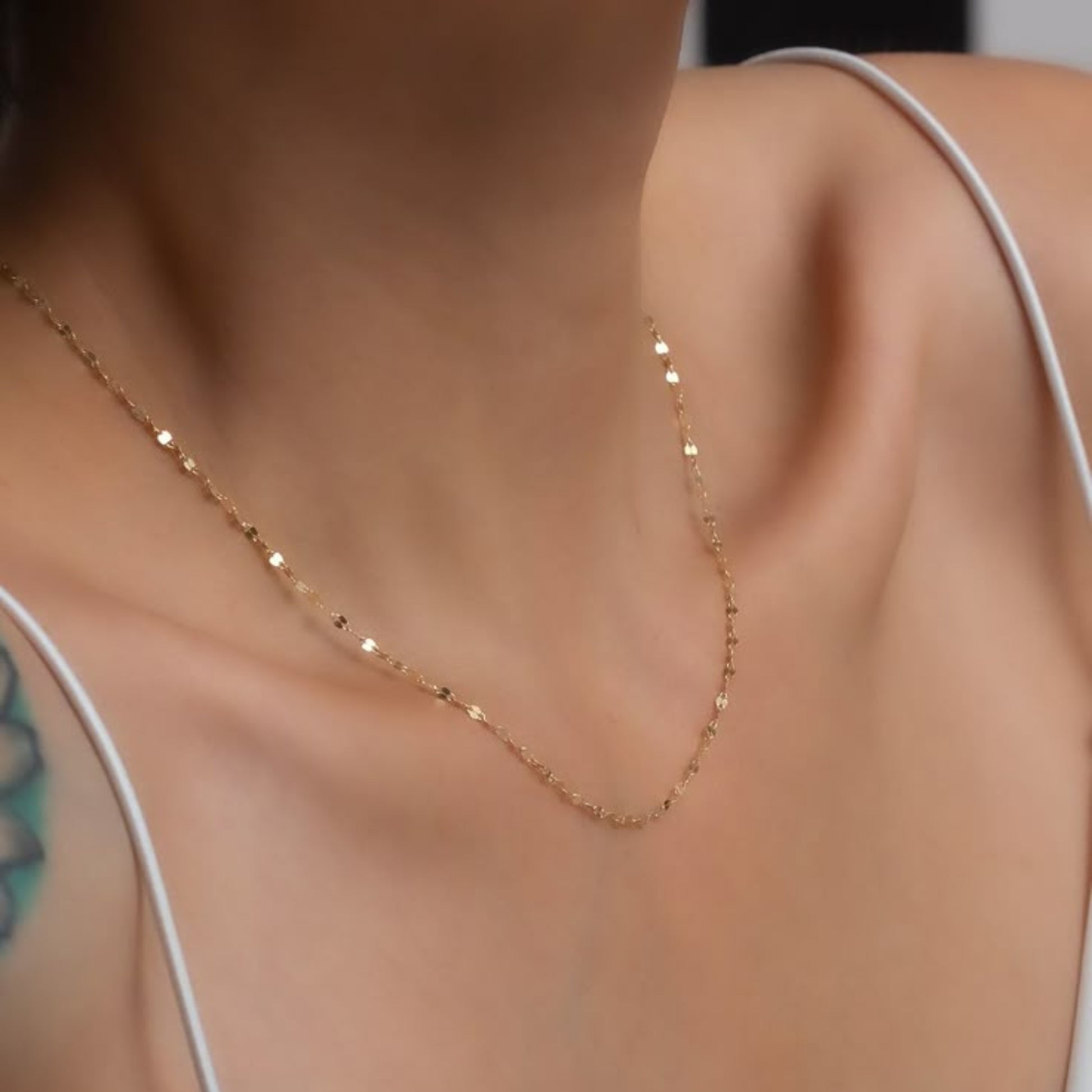 Gold necklace on a person wearing a white top