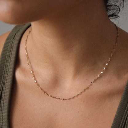Close-up of a person wearing a delicate gold necklace against a neutral background