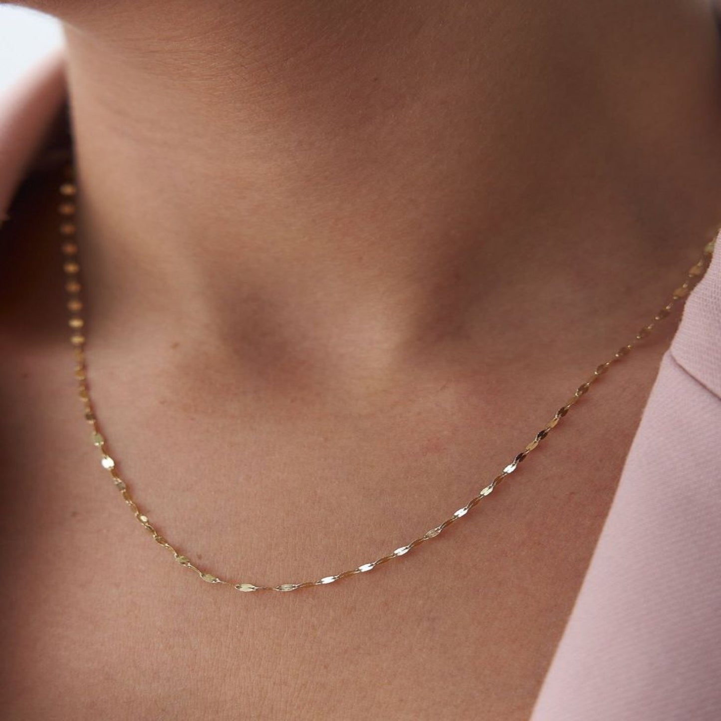 Gold necklace on a person's neck with a soft pink background