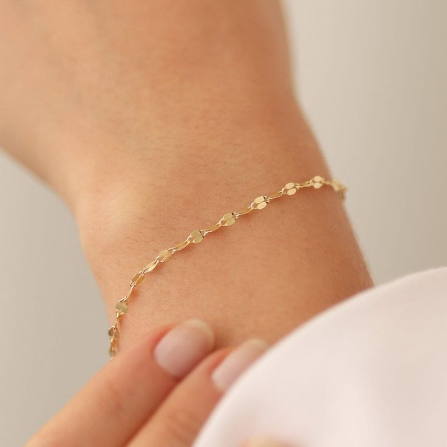 Gold bracelet on a wrist with a neutral background