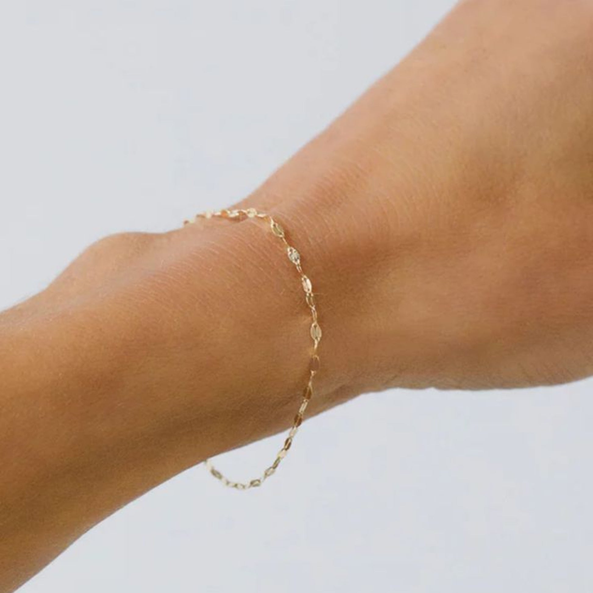 Gold anklet on a person's ankle against a light gray background