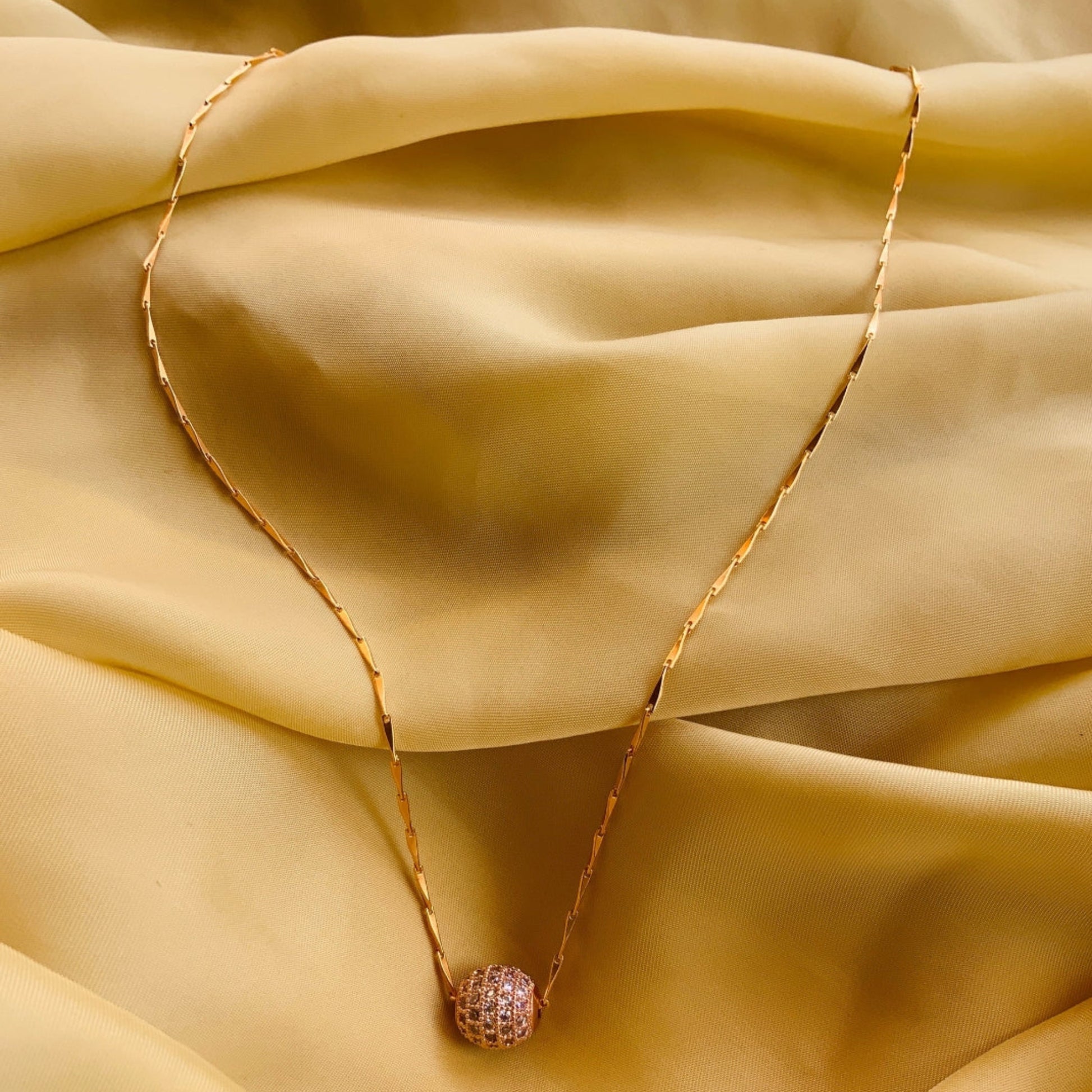 Gold necklace with a pink pendant on a beige fabric background