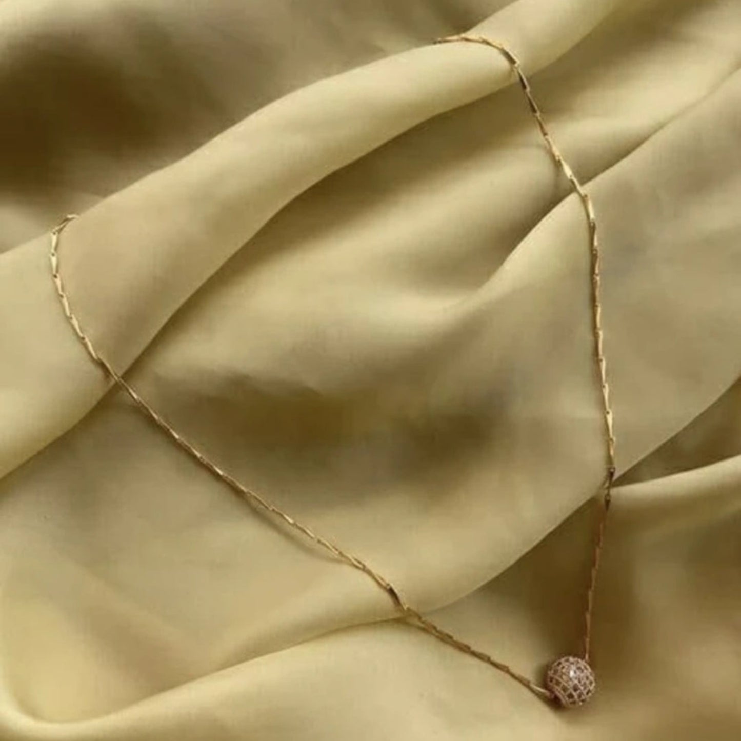 Necklace with a delicate chain and round pendant on beige fabric