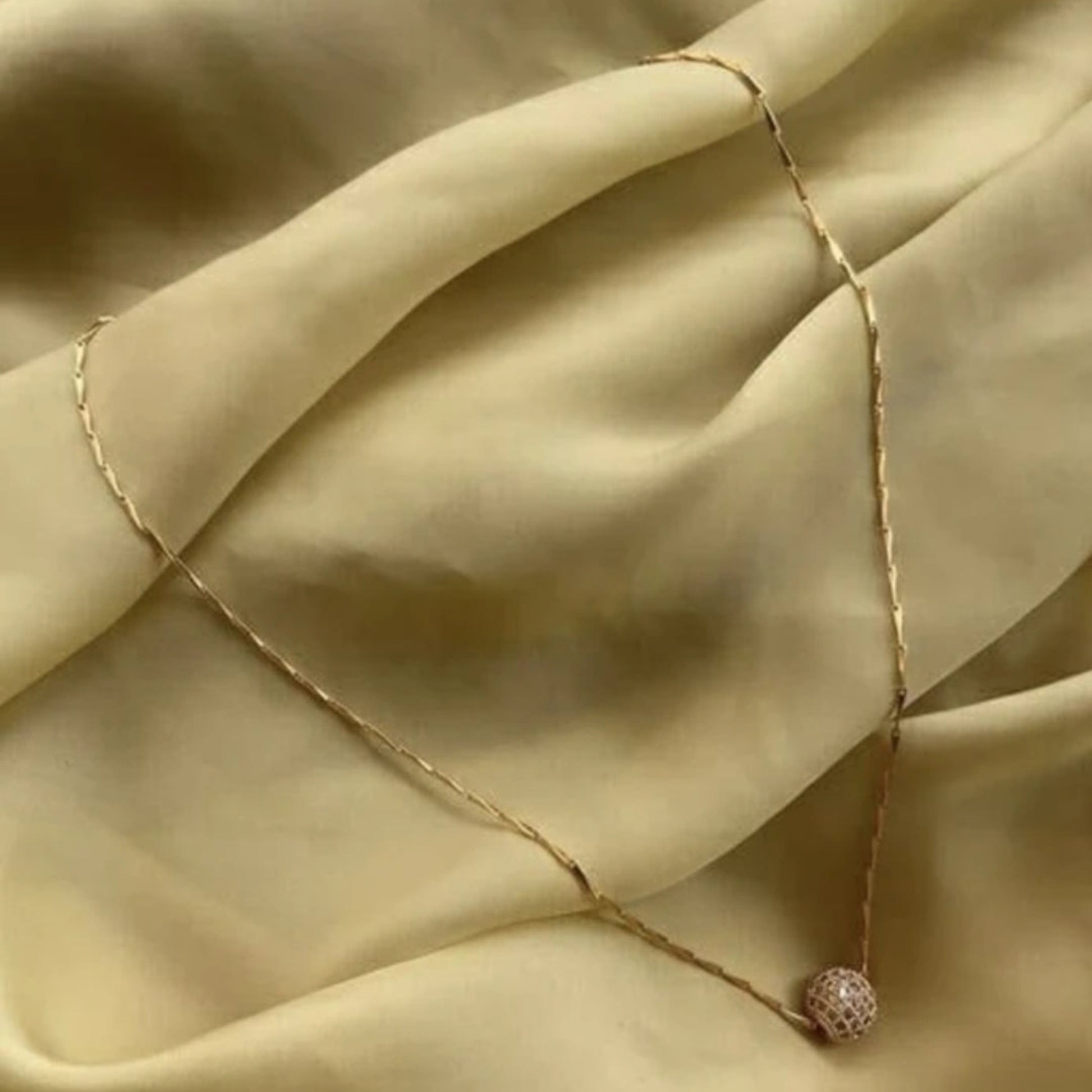 Necklace with a delicate chain and round pendant on beige fabric