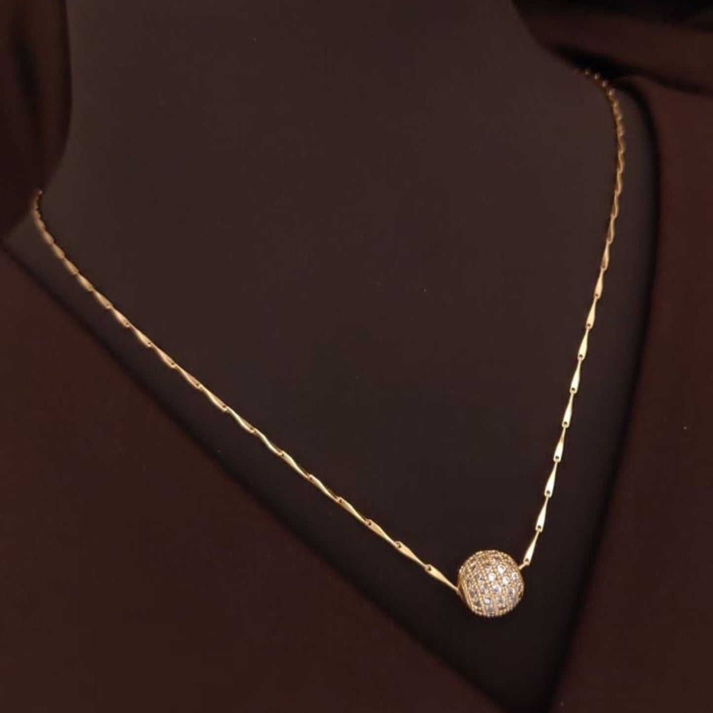 Gold necklace with a diamond pendant on a brown fabric background