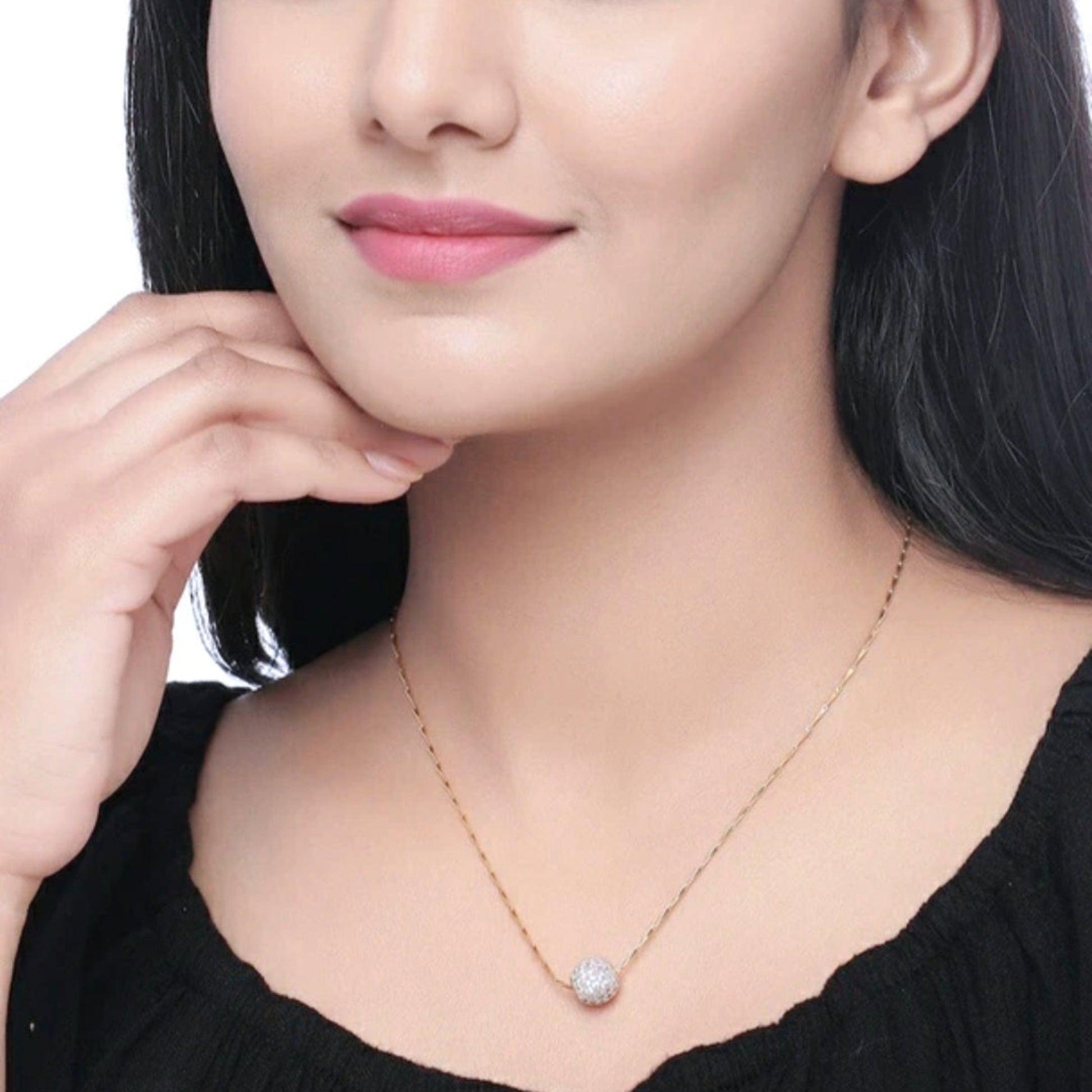 Woman wearing a delicate necklace with a clear pendant against a neutral background