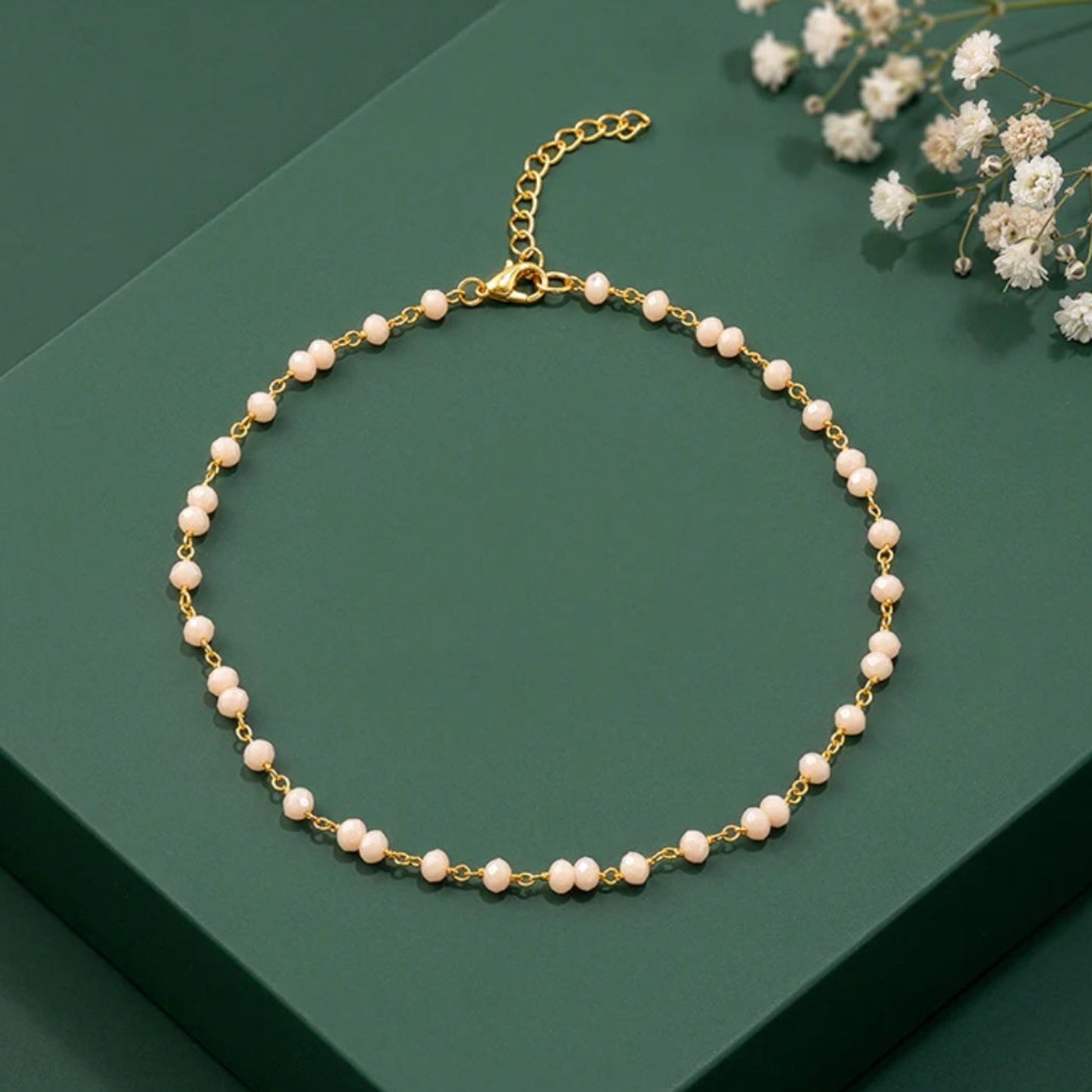 Pearl necklace with gold chain on a green surface with white flowers.