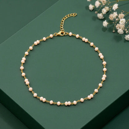 Pearl necklace with gold chain on a green surface with white flowers.