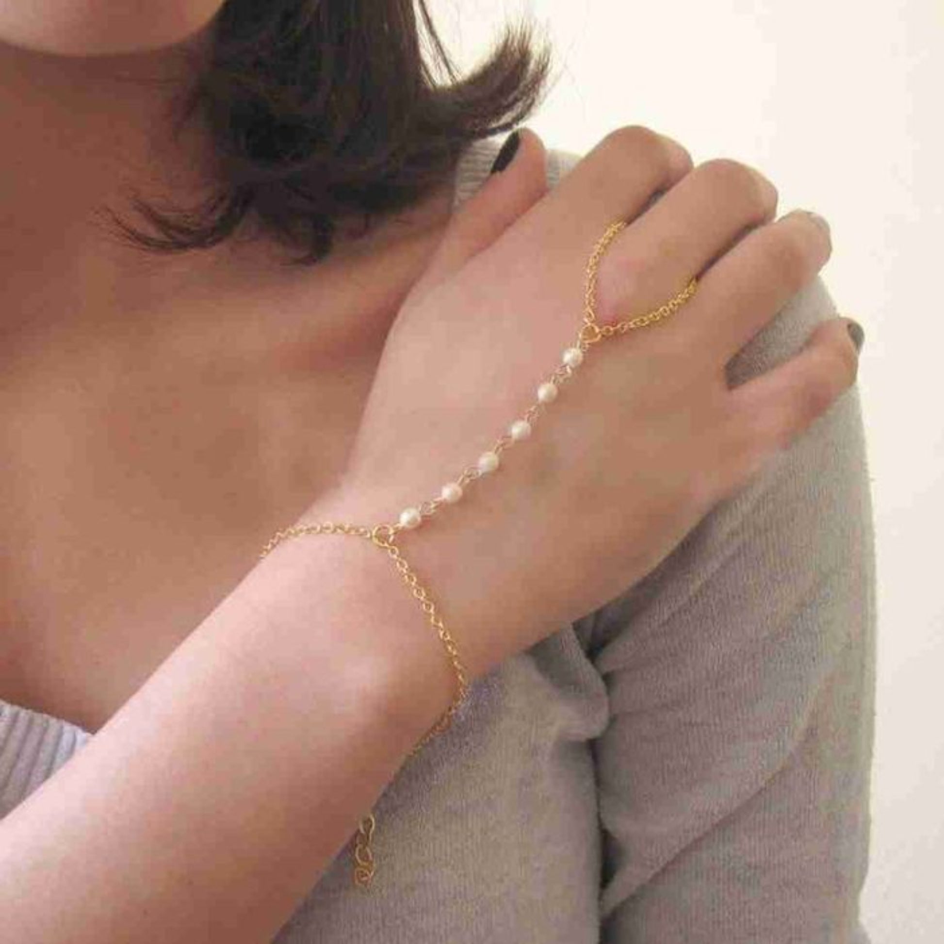 Gold bracelet with pearl beads on a person's wrist against a neutral background