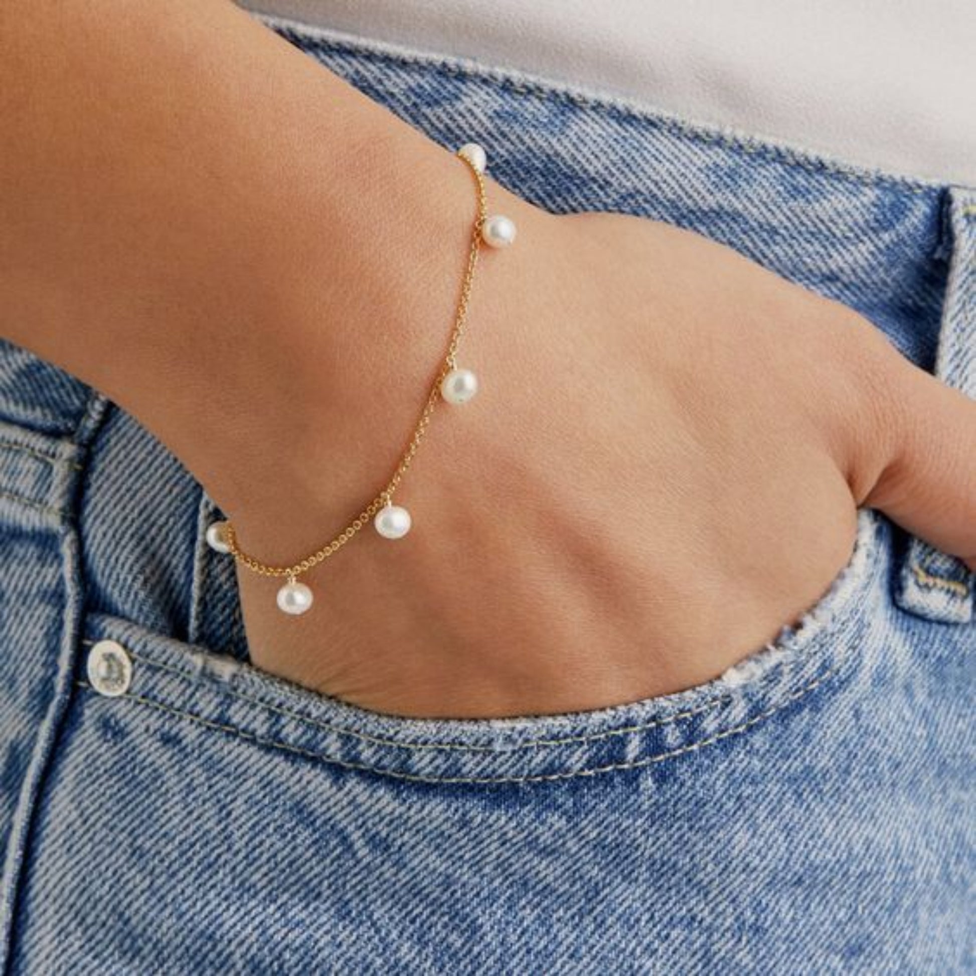 Gold bracelet with pearls on a wrist against a denim background